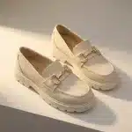 Mocassins femme chunky blanc en simili cuir. Vue studio sur fond neutre, montrant le détail du mors doré sur le dessus et la semelle épaisse crantée.