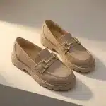 Paire de mocassins à plateforme couleur taupe clair. Chaussures de ville tendance avec boucle décorative dorée et grosse semelle crantée assortie.