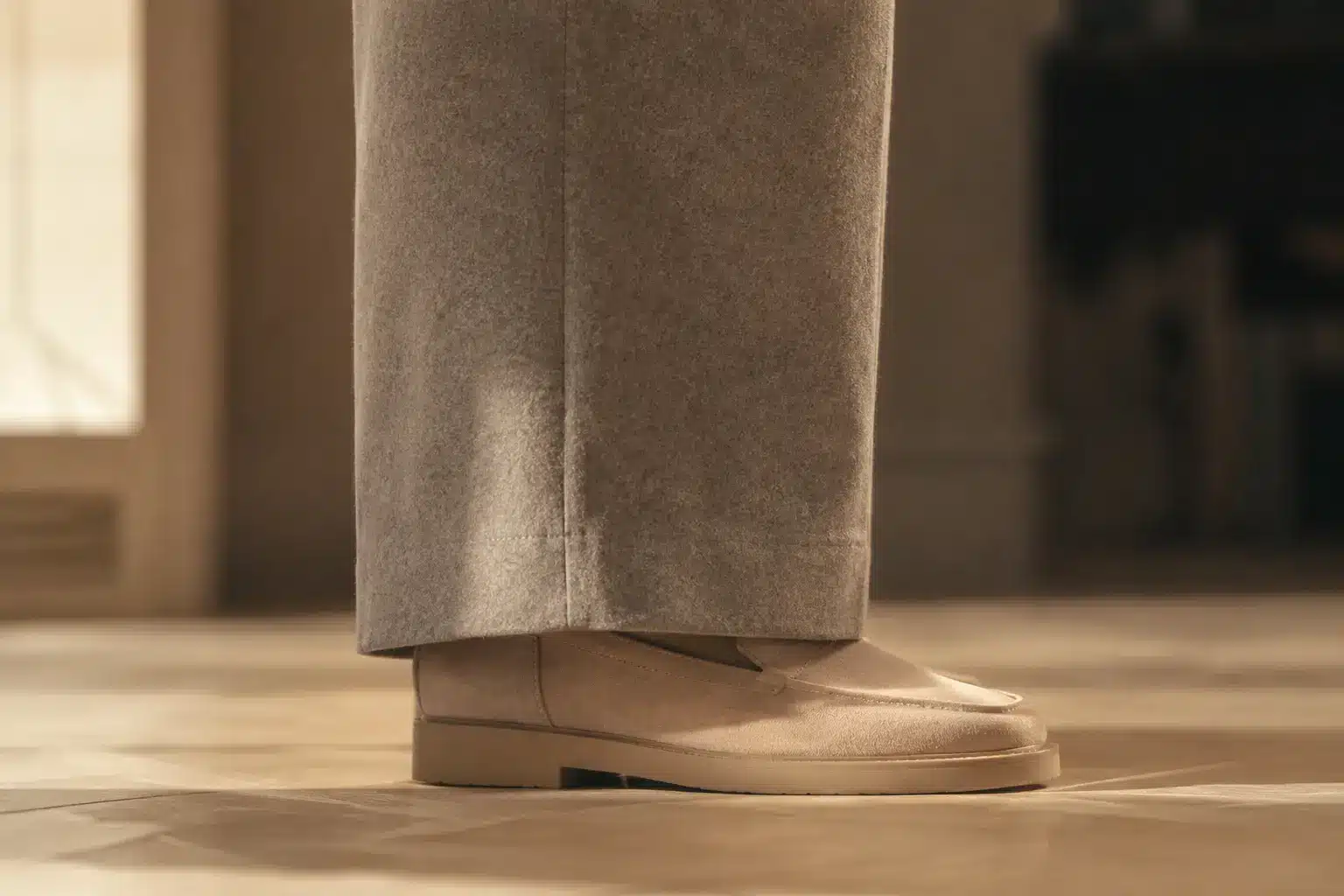 Ourlet d'un pantalon large en flanelle grise effleurant un mocassin en daim beige